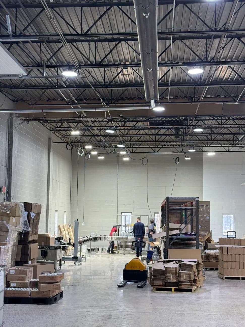 A warehouse work area lit by ceiling fixtures, with pallets and staff working below